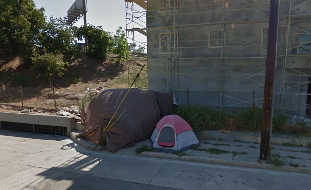 A grey and pink tent set up next to a brown tarp shelter on a grassy patch of sidewalk.