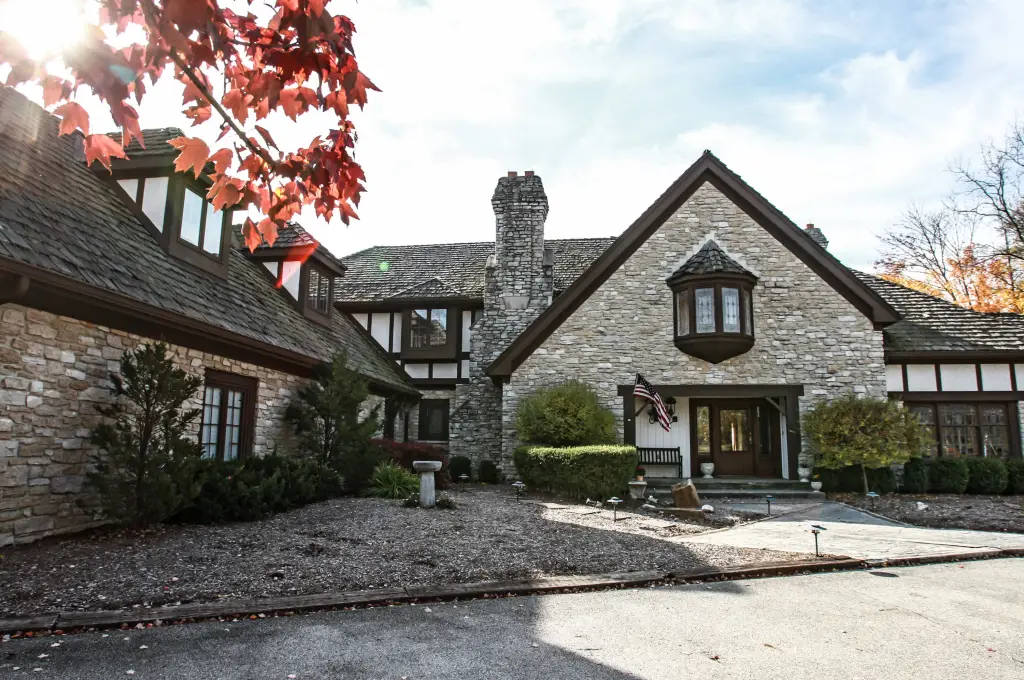 Frontal view of the Tudor-style Fox Hollow Farm main house with stone facade, dark wood trim, and an American flag near the entrance.
