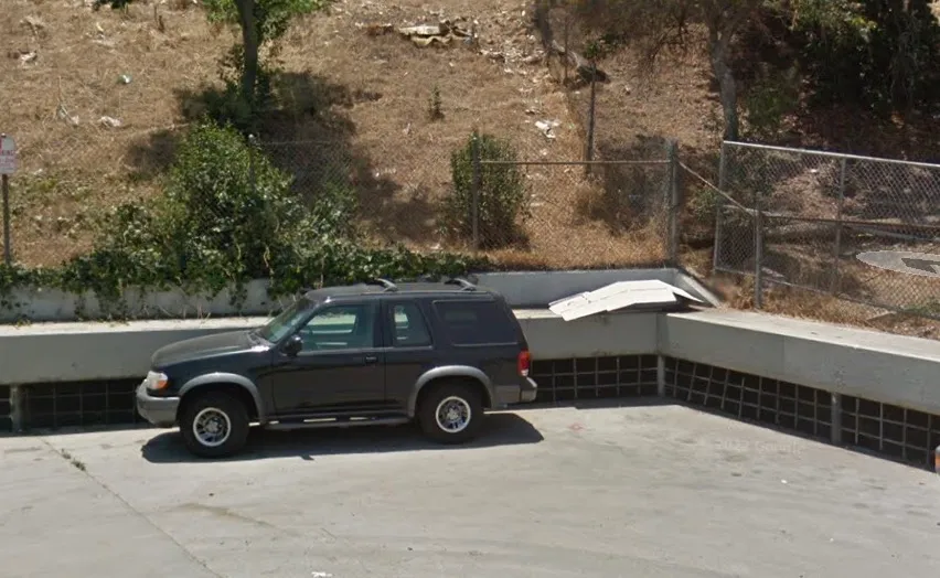 A black Ford Explorer SUV parked next to a concrete wall with a chain-link fence and dry hillside in the background.