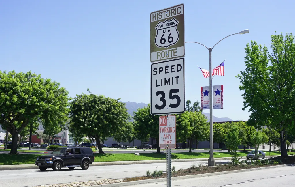 A Route 66 sign on Foothill Drive in Monrovia, California, with a 35 mph speed limit, next to American flags and banners for U.S. Army and Air Force veterans.