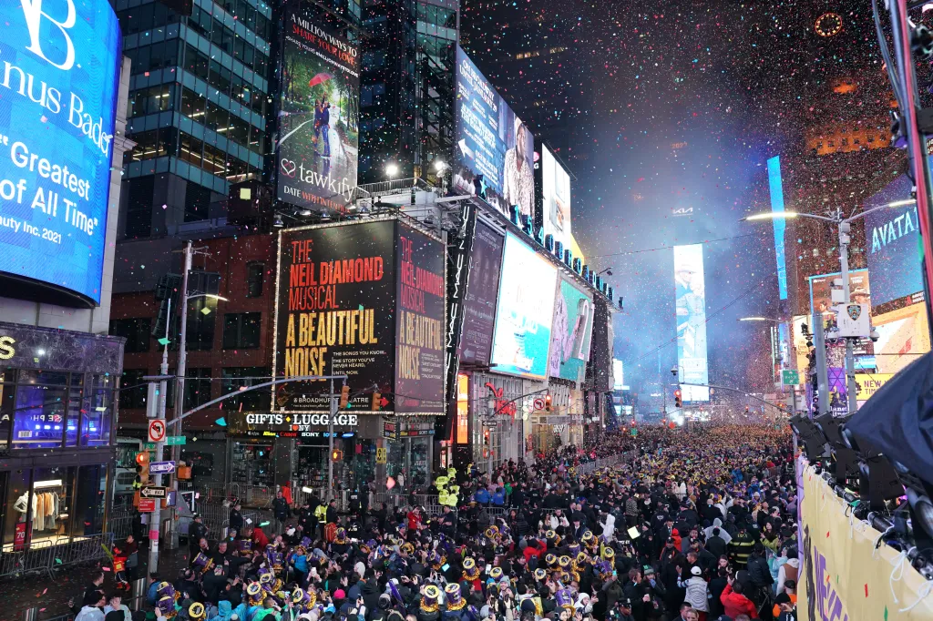 Confetti falls over a large crowd celebrating New Year's Eve 2023 in Times Square, New York City, surrounded by brightly lit billboards.