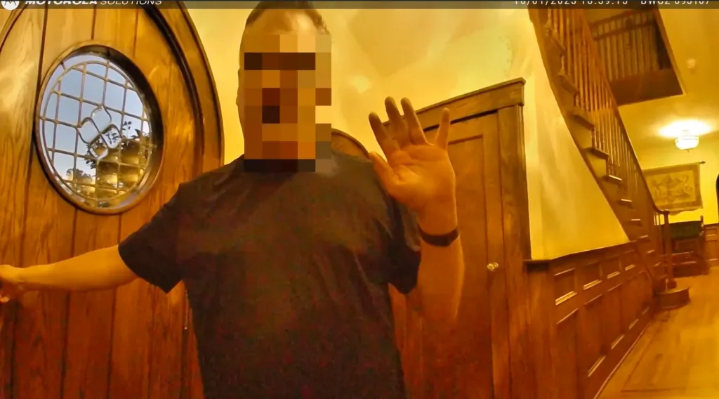 Police body-cam footage shows John Overdeck, face pixelated, in a wood-paneled room.