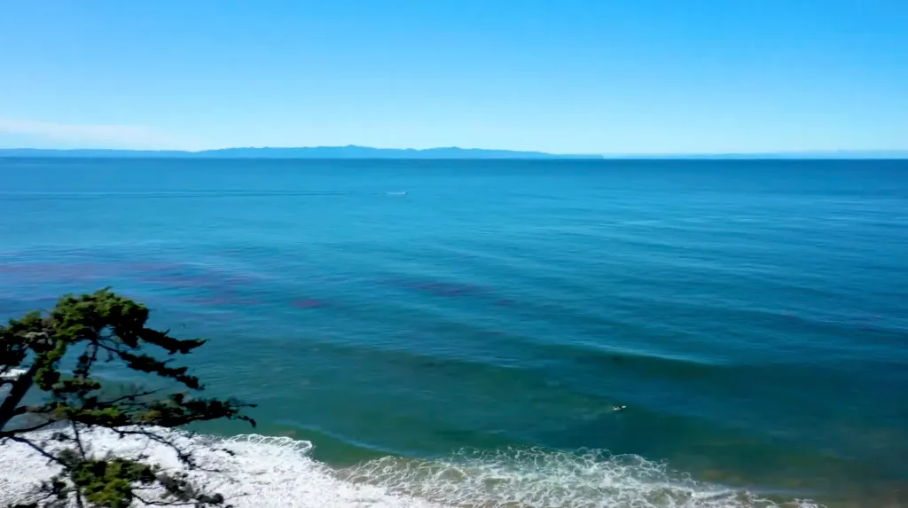 Ocean view with a distant landmass and foamy waves in the foreground.