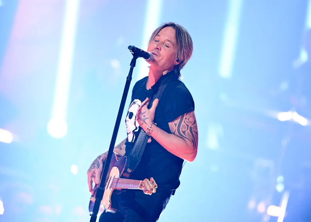 Keith Urban performing onstage, wearing a black shirt and holding a guitar.