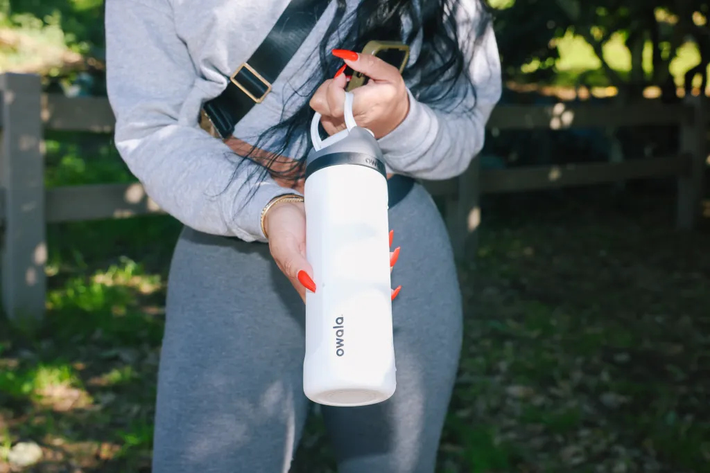 A person holding a white Owala water bottle with bright red manicured nails.