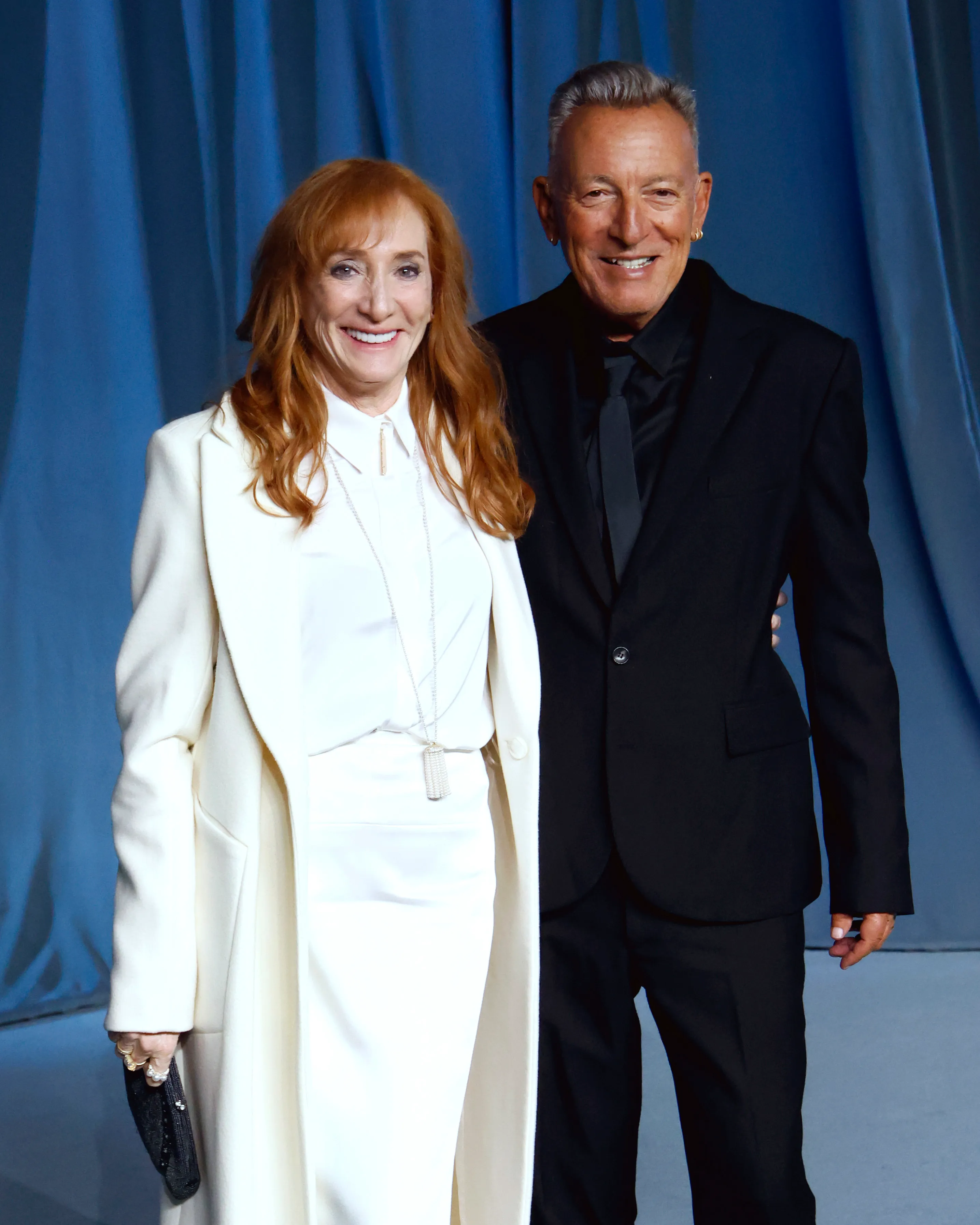 Patti Scialfa in a white outfit and Bruce Springsteen in a black suit smiling at the Academy Museum Gala.