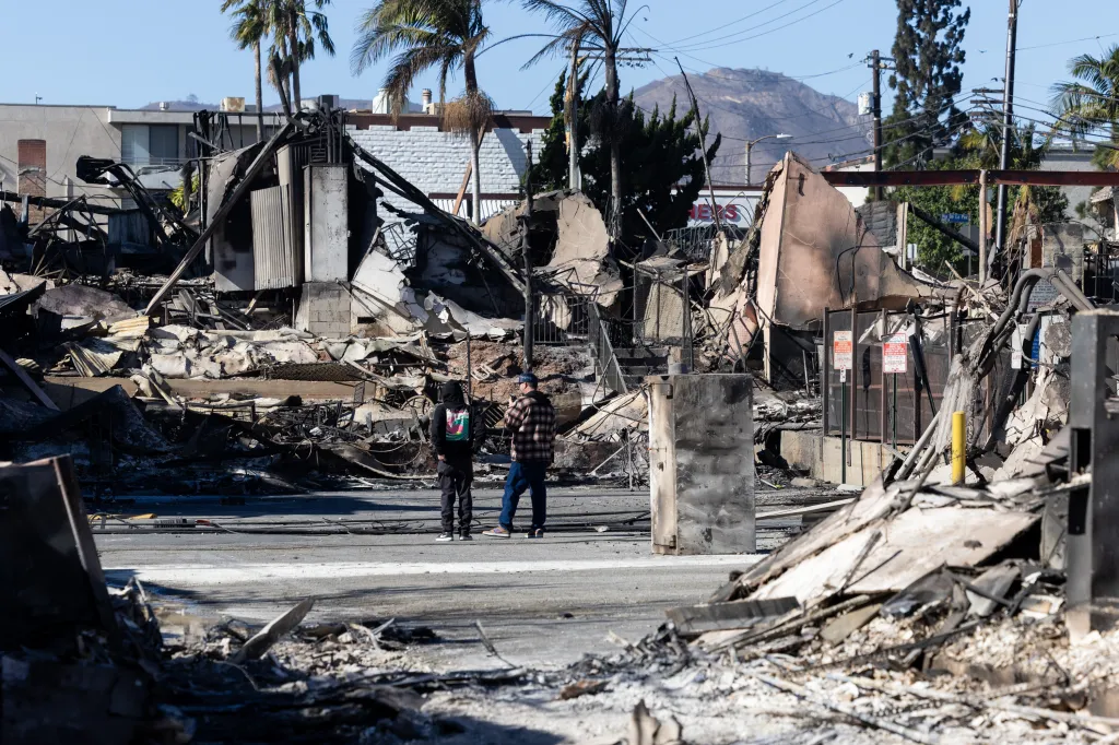 Two residents look at scorched buildings of a shopping mall after wildfires in the Pacific Palisades neighborhood of Los Angeles.