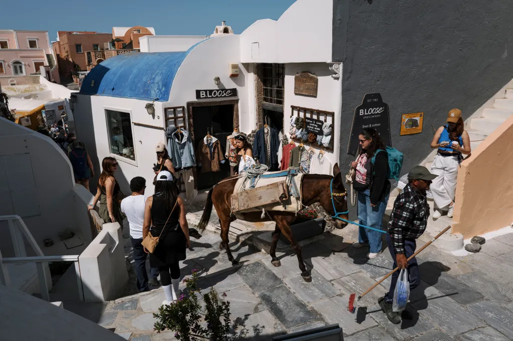 A resident leads a donkey past tourists in Oia village on Santorini, Greece.