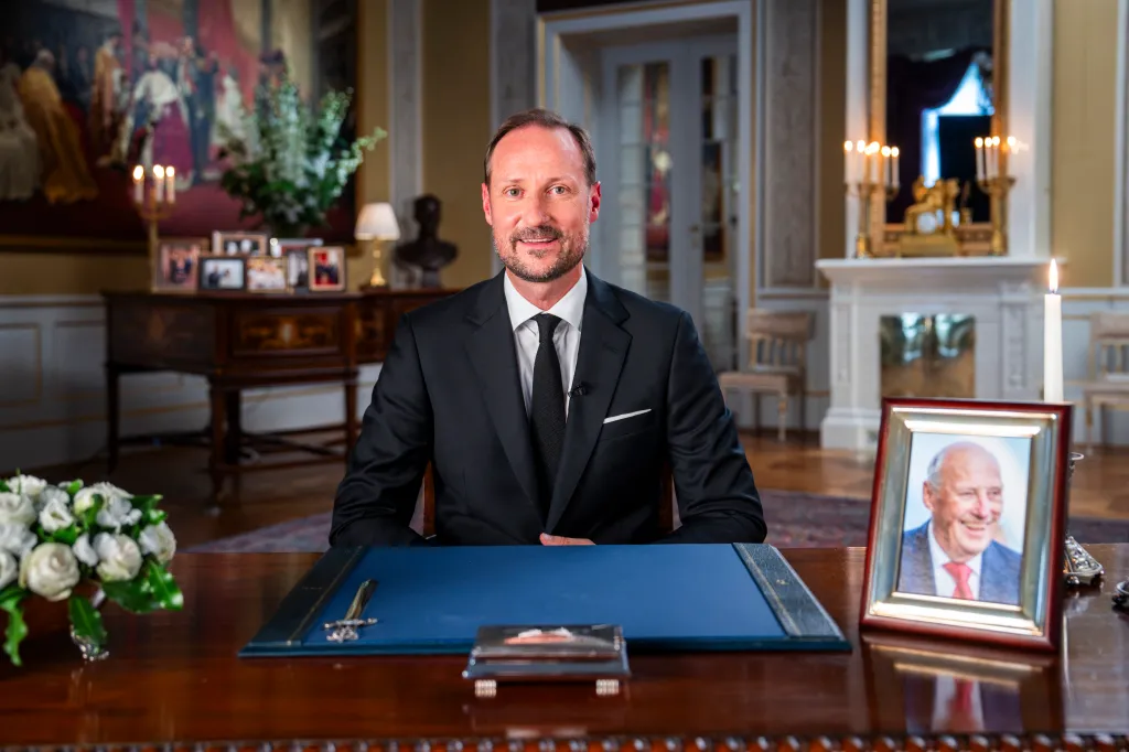 King Haakon VIII of Norway sits at a desk, delivering his first speech to the nation.