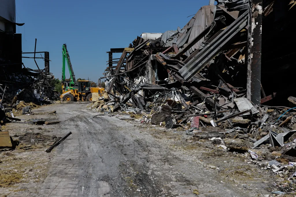 A damaged shopping mall in Kryvyi Rih, Ukraine, following a Russian strike, with debris scattered and a construction vehicle in the background.