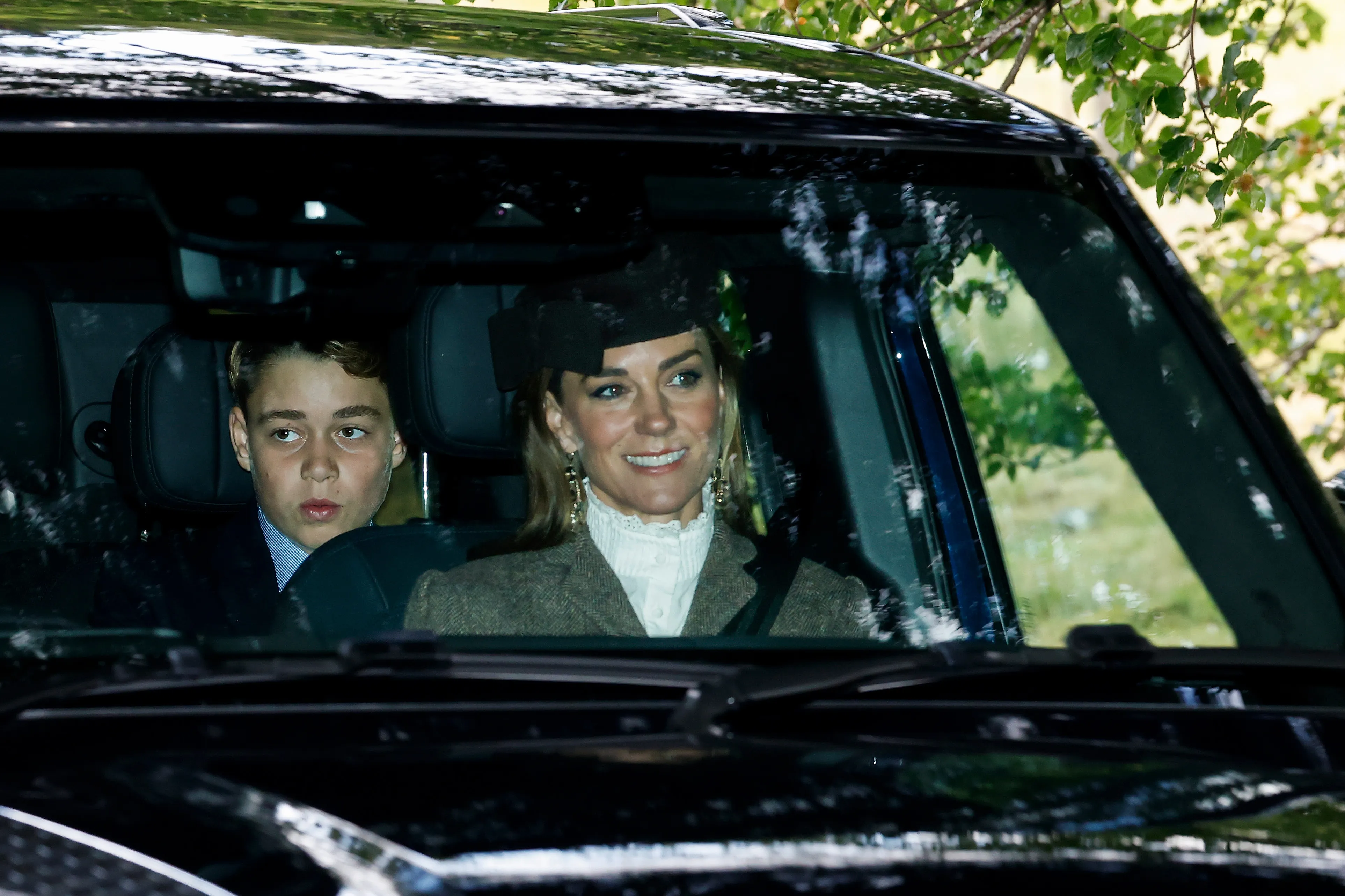 Catherine, Princess of Wales, smiles from the passenger seat of a car, with Prince George visible in the back seat.