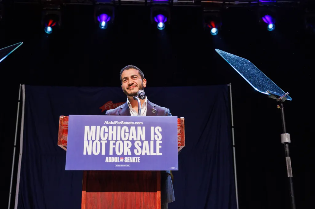 Abdul El-Sayed speaking at a podium with a sign that reads 
