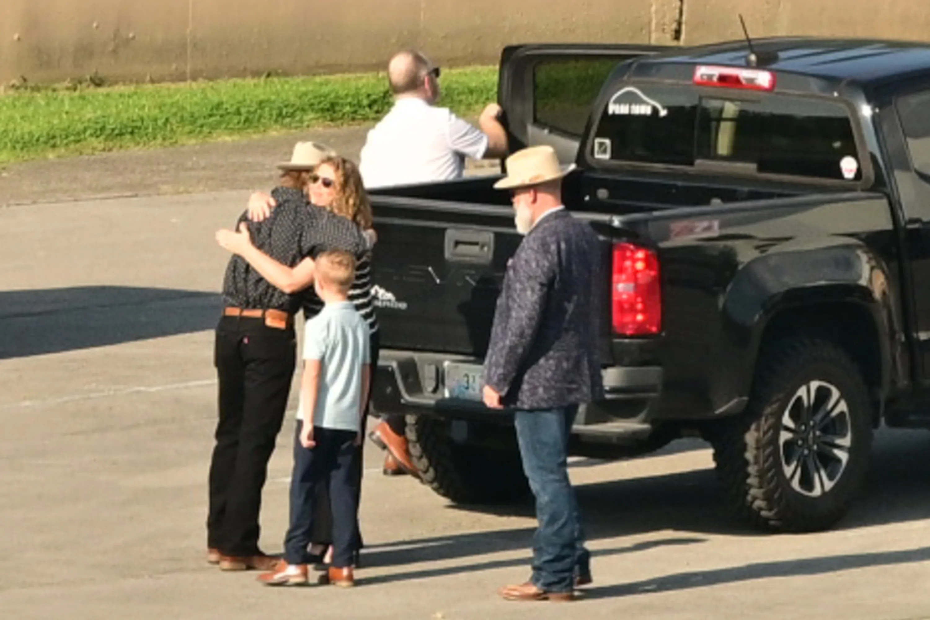 A group of people embracing near a black pickup truck.