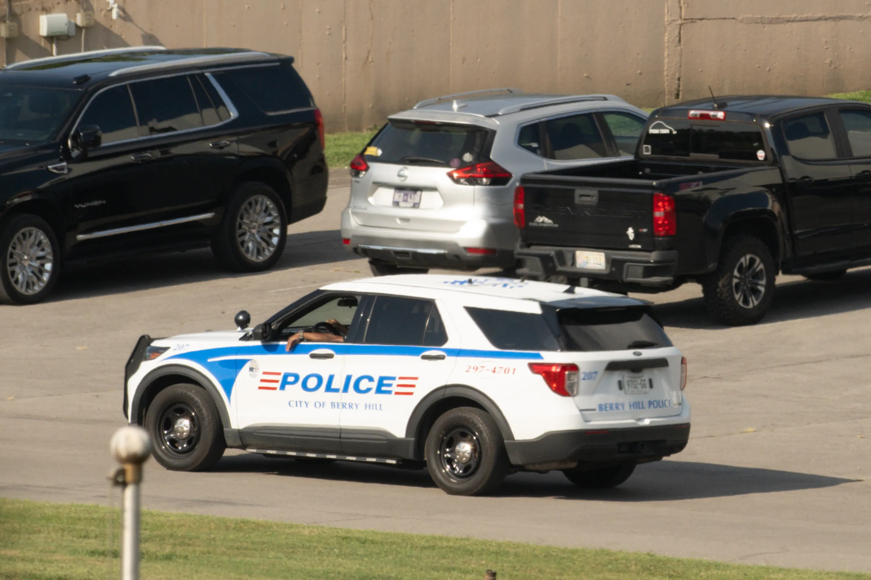A police car, parked among other vehicles, with a driver's arm resting on the open window.