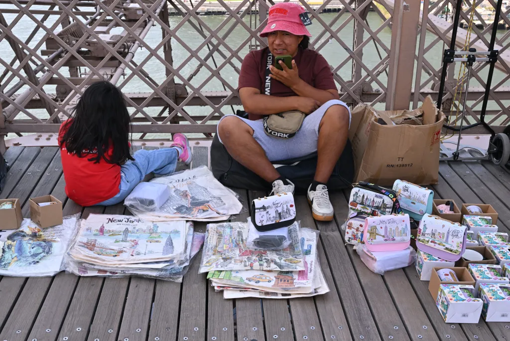 A man and a child selling New York-themed merchandise on the Brooklyn Bridge pedestrian walkway.