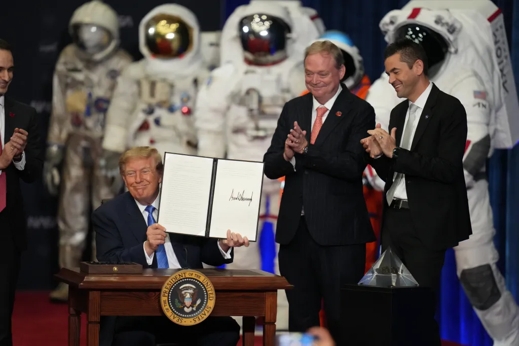 President Donald Trump at a Congressional Space Medal of Honor ceremony with Kevin Hassett and Jared Isaacman, in front of several space suits.