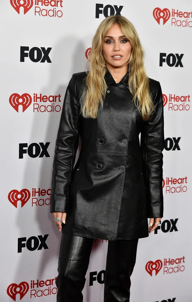 Miley Cyrus in a black leather coat and pants on the red carpet of the iHeartRadio Music Awards.
