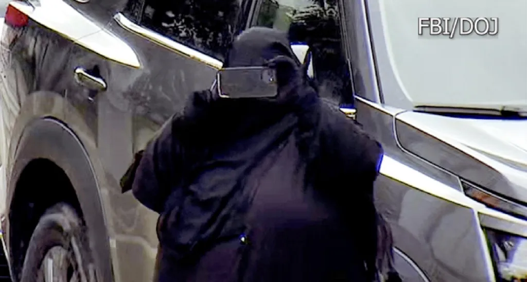 Jessica Bowie in a black niqab holding a phone to record a dark SUV.