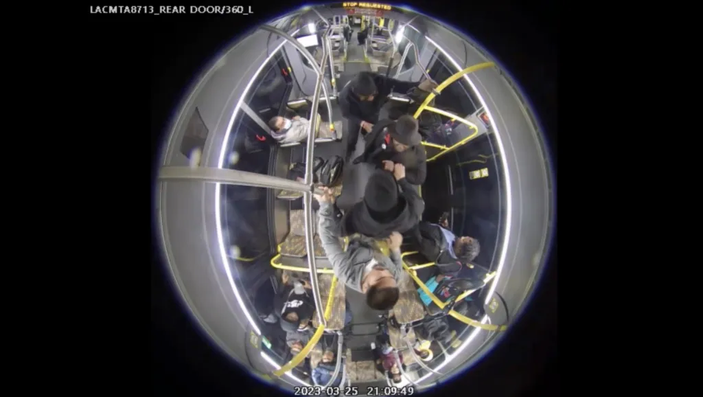 Fisheye view from a bus security camera showing several people standing and sitting inside the bus.