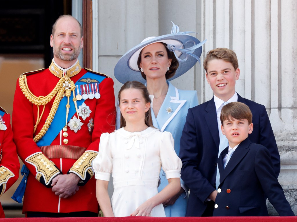 Prince William, in a red military jacket, with blue sash and medals, Kate Middleton in a blue coat with white trim and matching hat, Princess Charlotte, in a white dress, Prince George and Prince Louis in blue suits, at Trooping the Colour 2026.