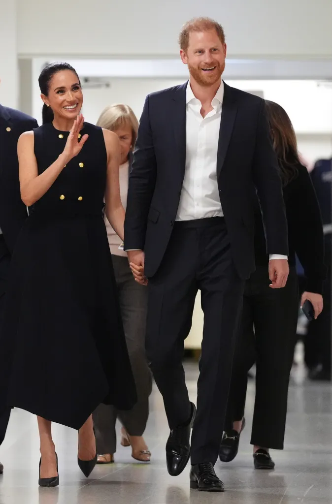 Meghan, Duchess of Sussex, and Prince Harry, Duke of Sussex, smiling and holding hands while walking.