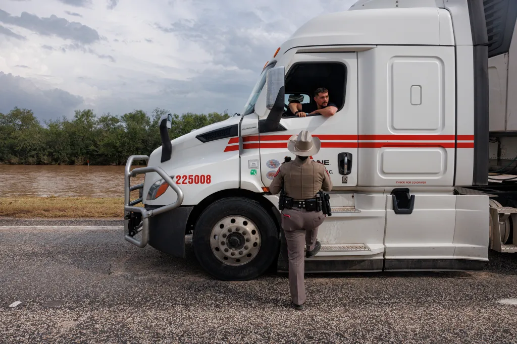 A Texas Department of Public Safety Trooper talks to truck driver Caleb Miller as floodwaters rise beside the road.