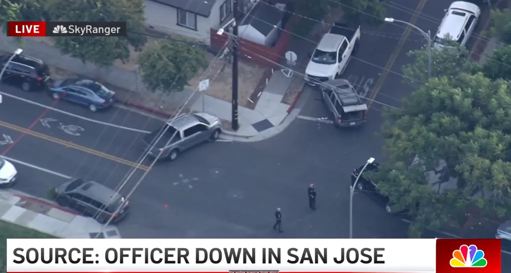 Aerial view of a street in San Jose with several vehicles, including police cars, and two officers on foot, after a police officer was shot.