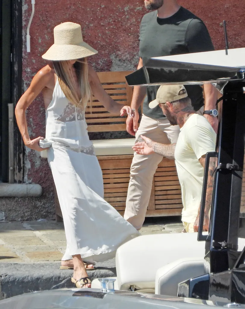 Victoria Beckham in a white backless dress and straw hat, holding a camera, as David Beckham plays photographer.