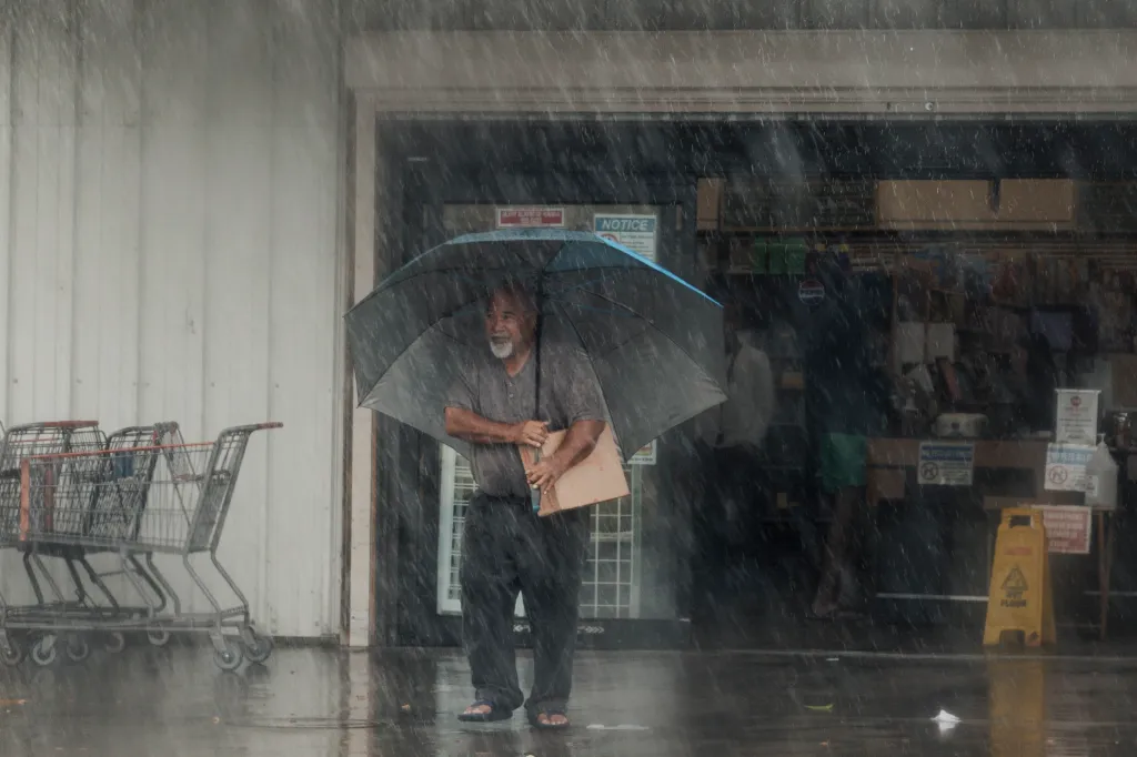 A man holding an umbrella carries supplies out of a store as Hurricane Lala strikes Hawaii on Aug. 15, 2026.