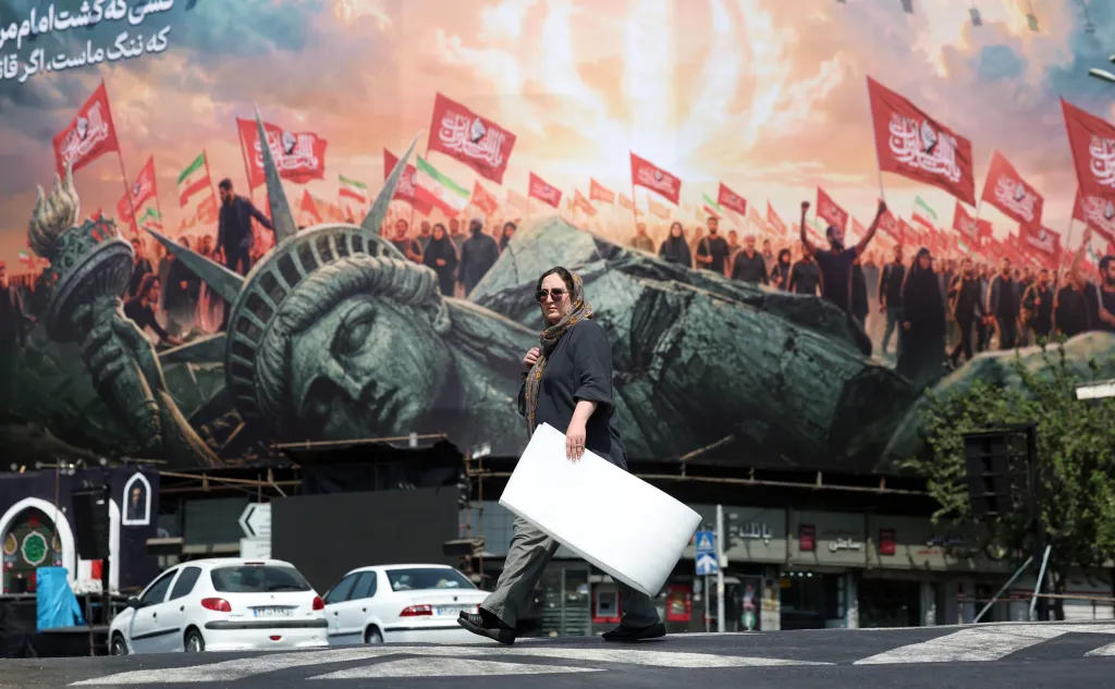 An Iranian woman walks past a billboard depicting the fallen Statue of Liberty and people holding flags in Tehran.