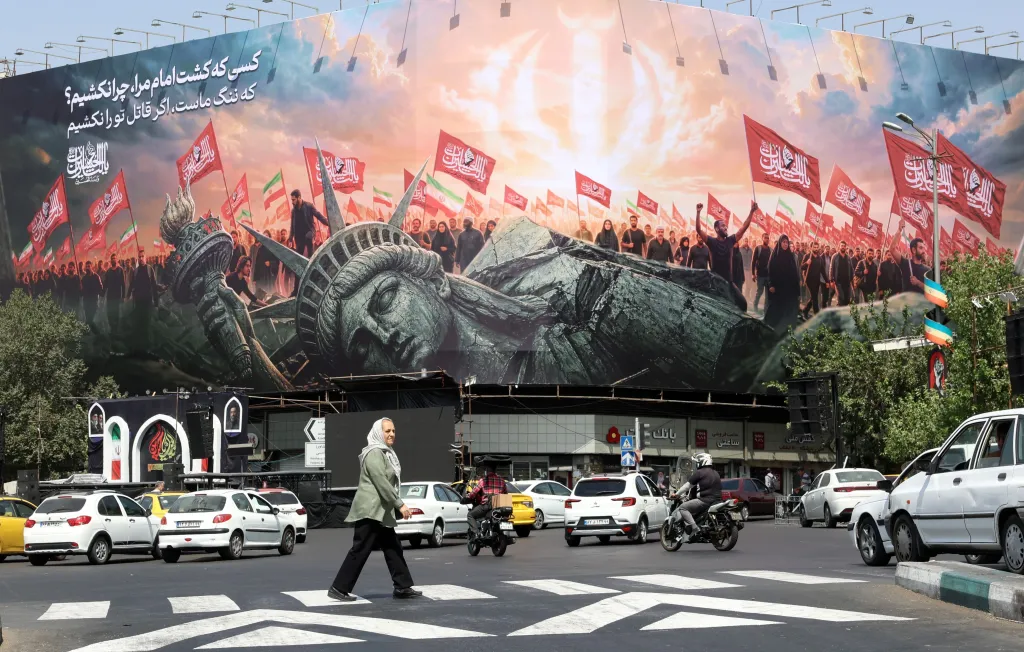 An Iranian woman walks past a billboard depicting the Statue of Liberty broken and surrounded by marching people carrying flags, at Enghelab Square in Tehran.