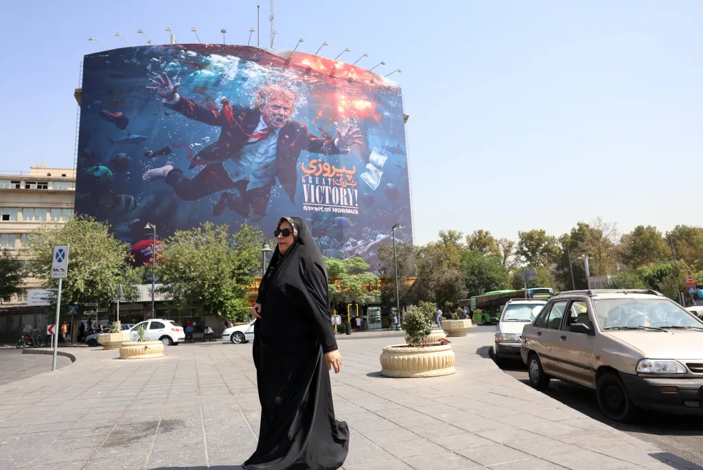 A veiled Iranian woman walks past an anti-US billboard featuring Donald Trump drowning, titled