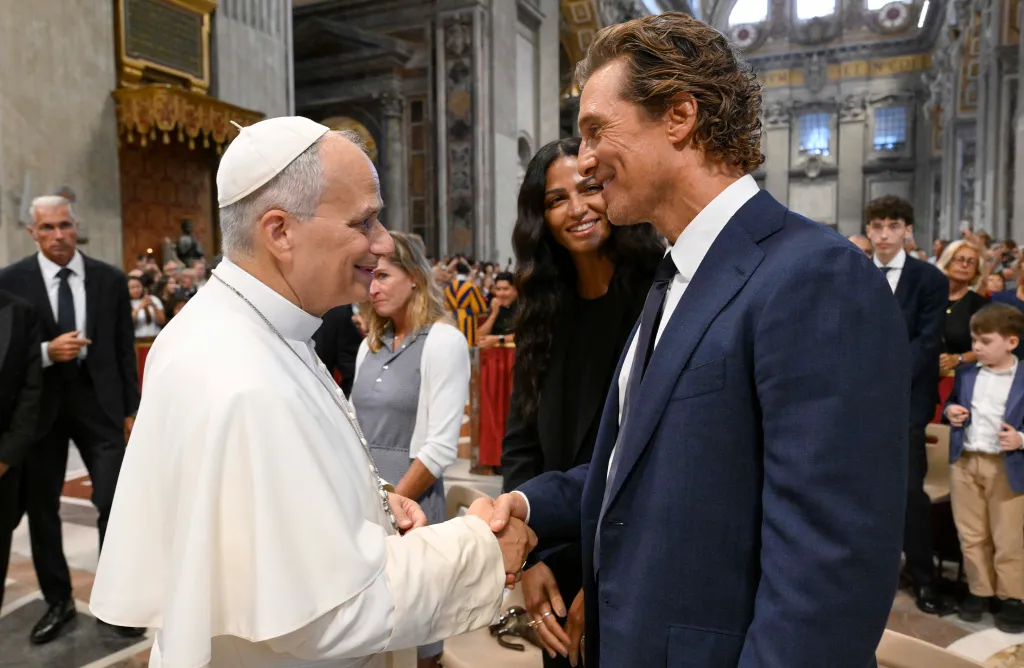 Pope Leo XIV shaking hands with Matthew McConaughey, while Camila Alves stands smiling behind McConaughey.