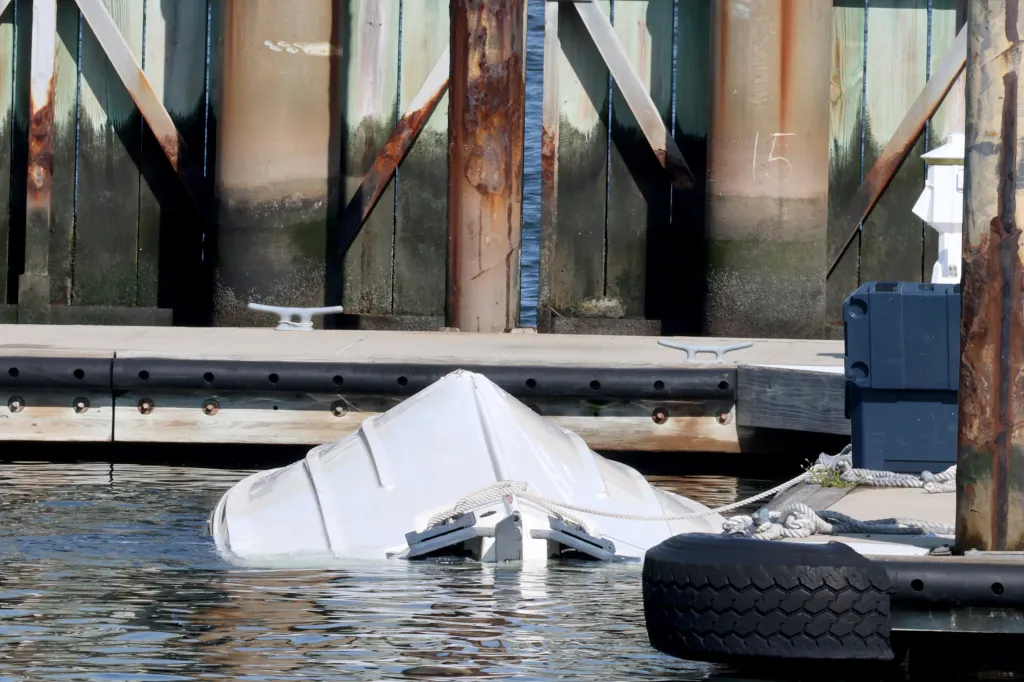 An overturned white boat floats partially submerged next to a dock.