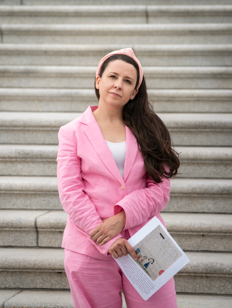 Ms. Rachel in a pink suit, holding letters from detained children, standing in front of the U.S. Capitol.