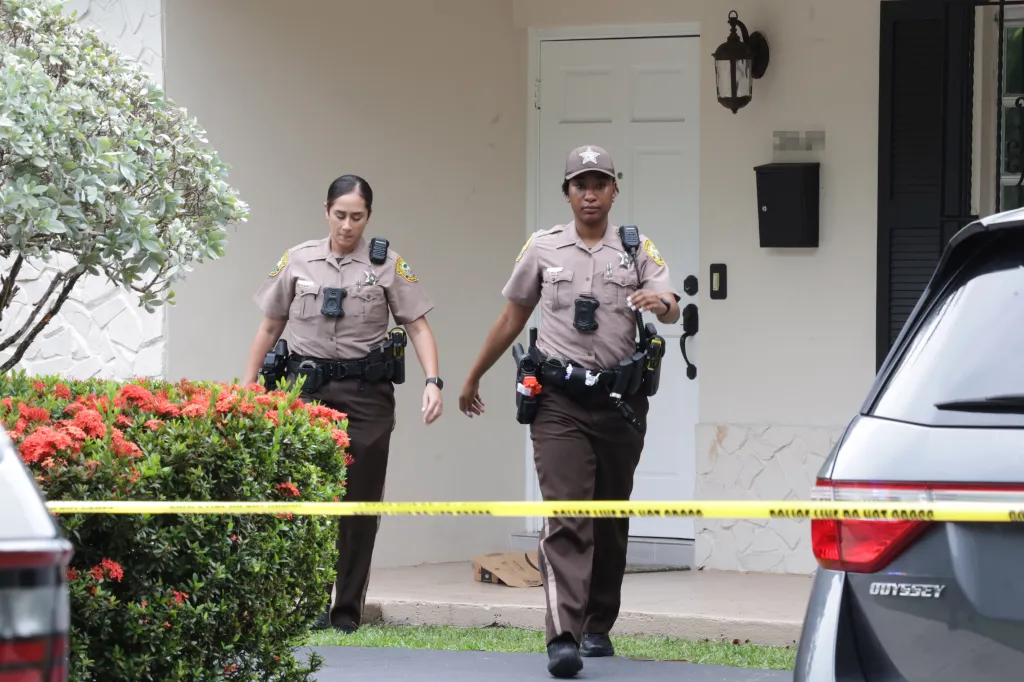 Two Miami-Dade County Sheriff's deputies walk past a yellow police line tape at the home of Perez Hilton.