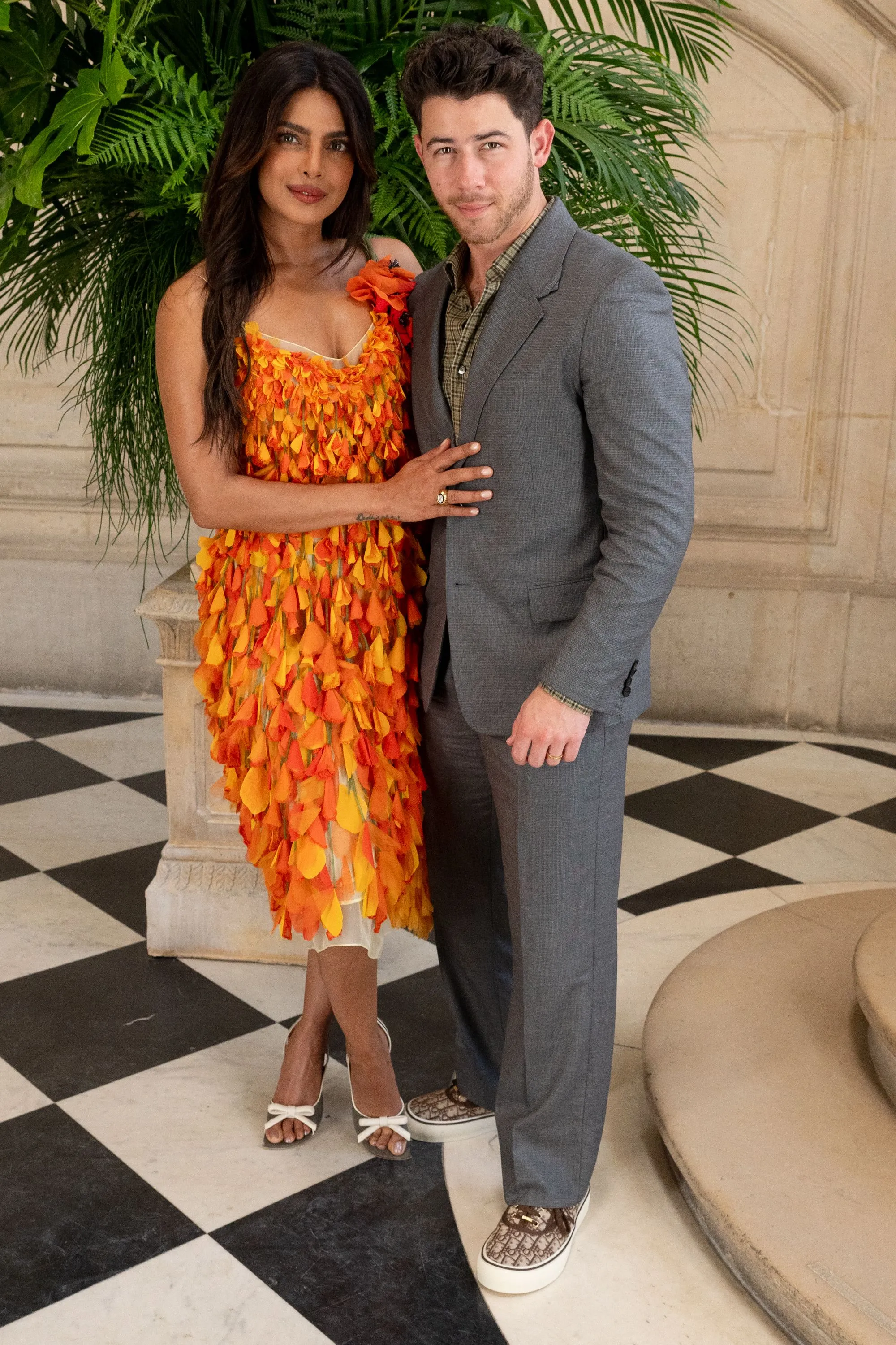 Priyanka Chopra in an orange and yellow petal dress with Nick Jonas in a gray suit at Paris Fashion Week.