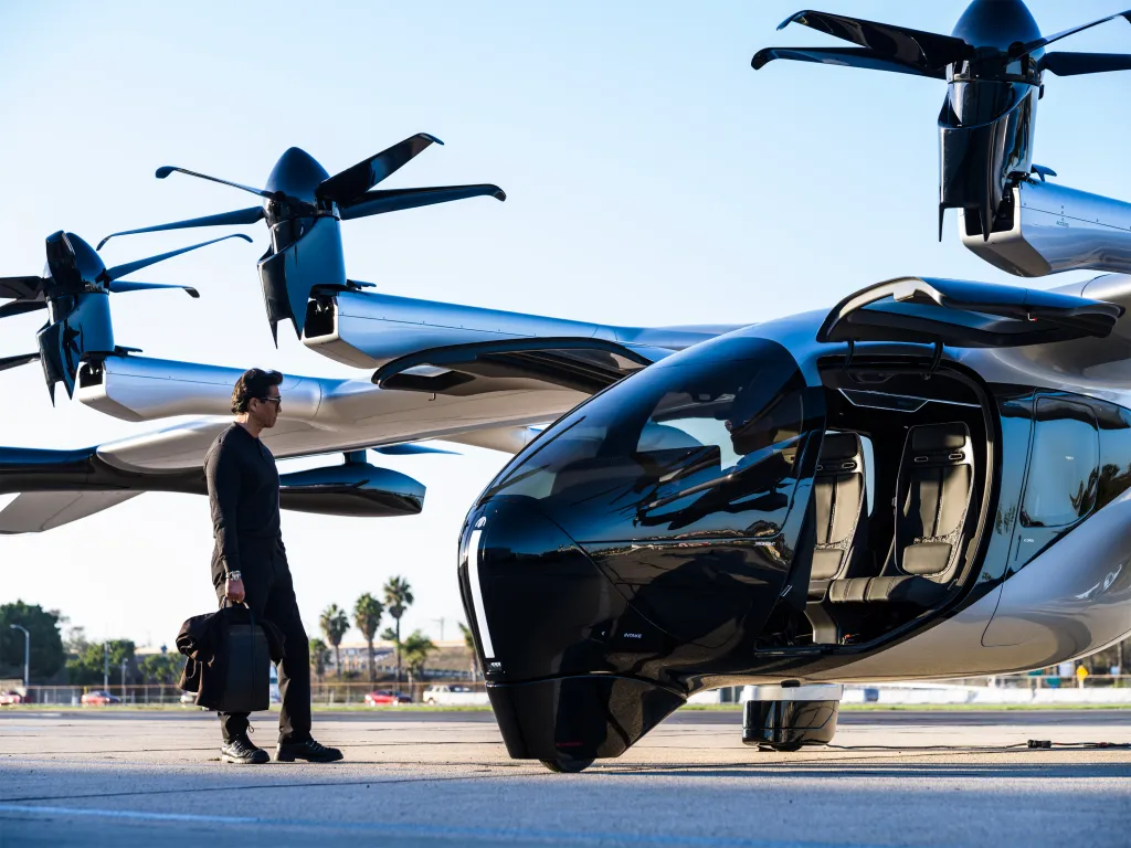 A man in a black outfit stands next to Archer Aviation's Midnight air taxi, which has its side door open.