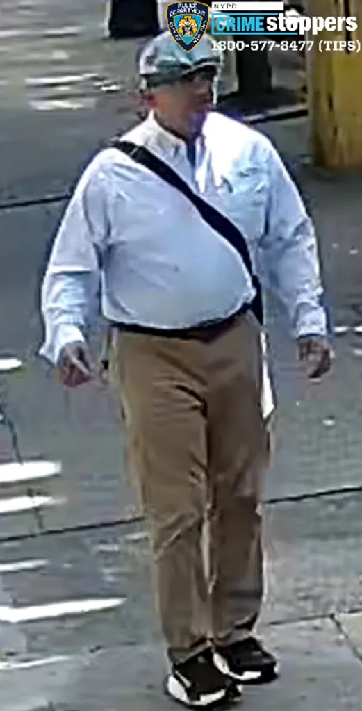 Surveillance photo of a man in a light blue long-sleeved shirt, tan pants, and a light-colored flat cap, walking on a sidewalk.
