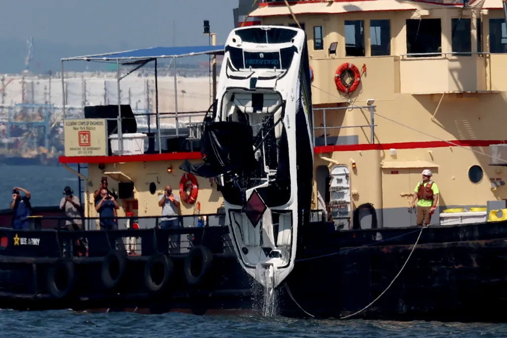 An overturned bowrider motorboat is lifted from the water by a crane vessel.