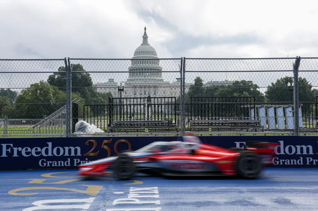 Red and white IndyCar racing past the U.S. Capitol building during the Freedom 250 Grand Prix practice laps.