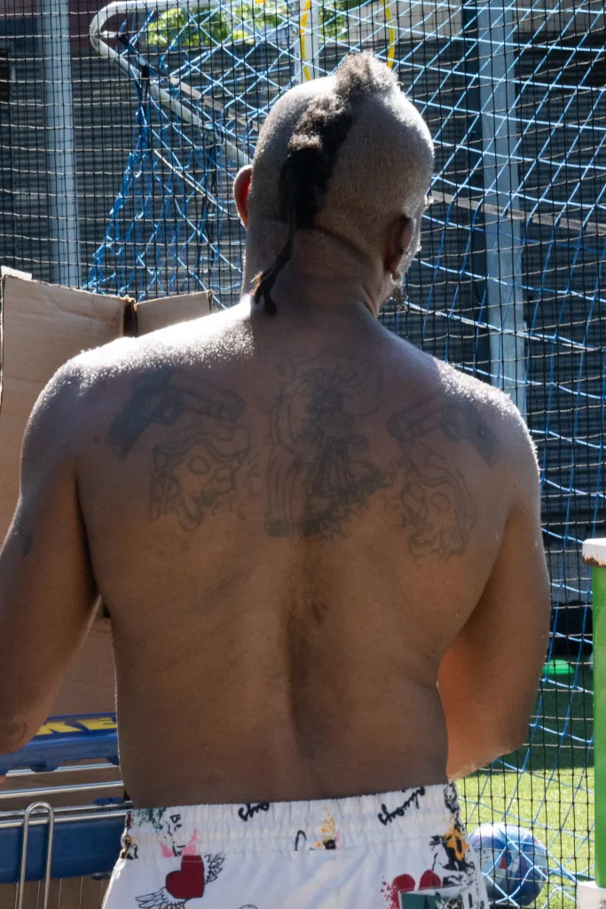 A person with a penis mask and tattoos on their back, viewed from behind on a soccer field.