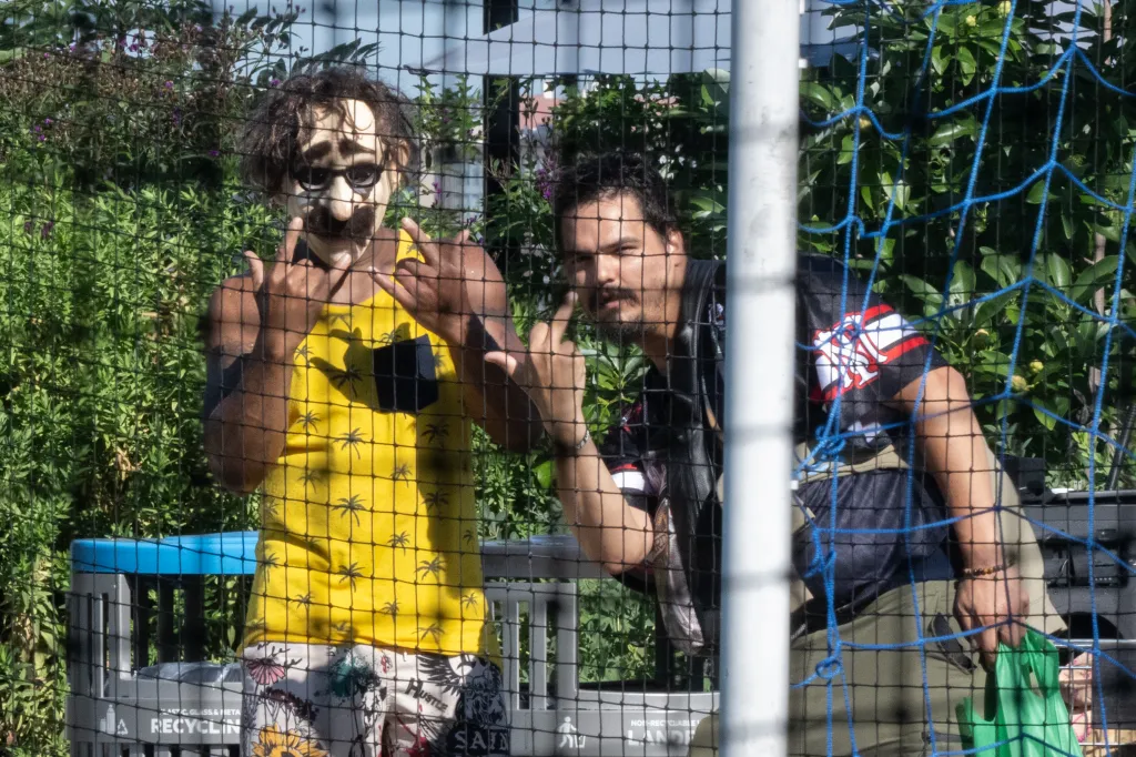 Two people behind a fence, one in a Groucho Marx mask giving 