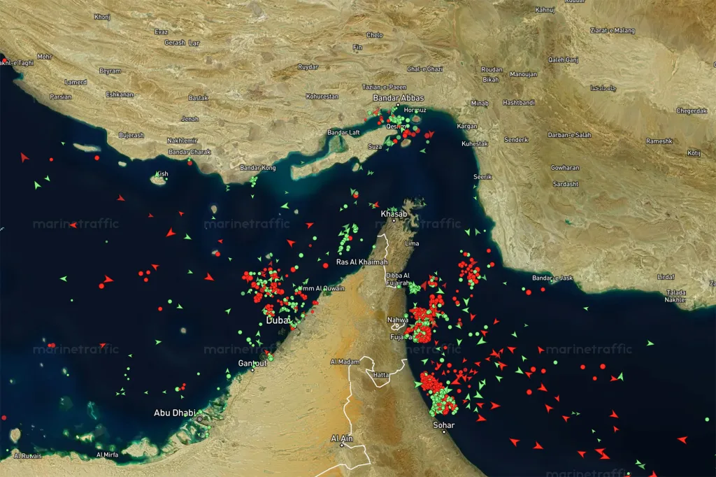 Satellite map showing marine traffic in and around the Strait of Hormuz, with green dots and red triangles indicating vessels.