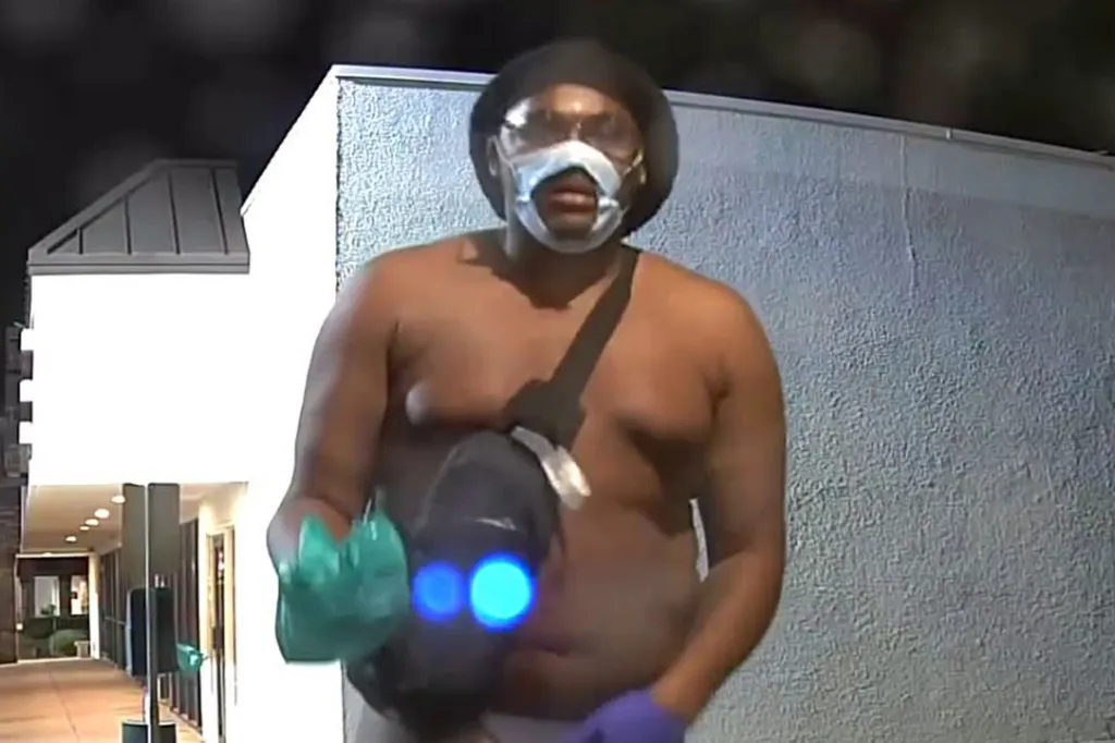 Still image of a man wearing a bucket hat, safety goggles, and a face mask over his mouth.