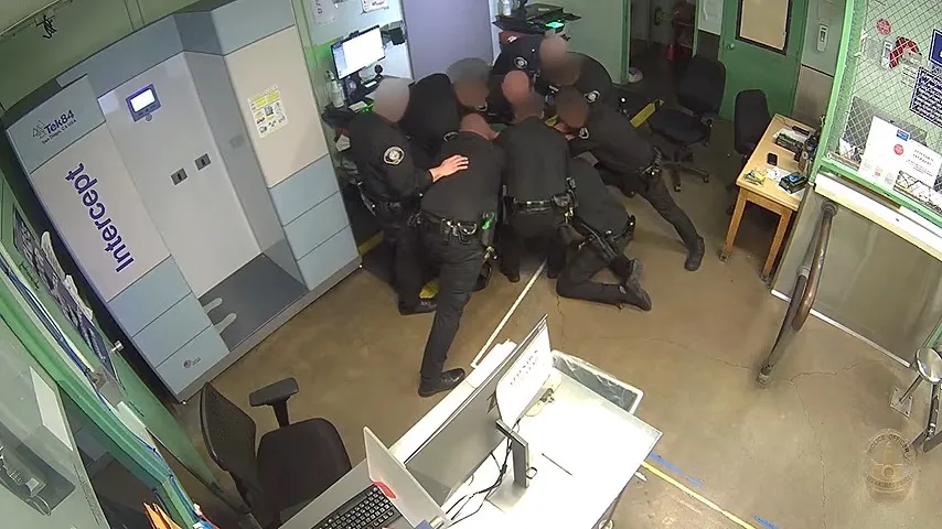 Police officers subduing a suspect on the ground next to a body scanner.