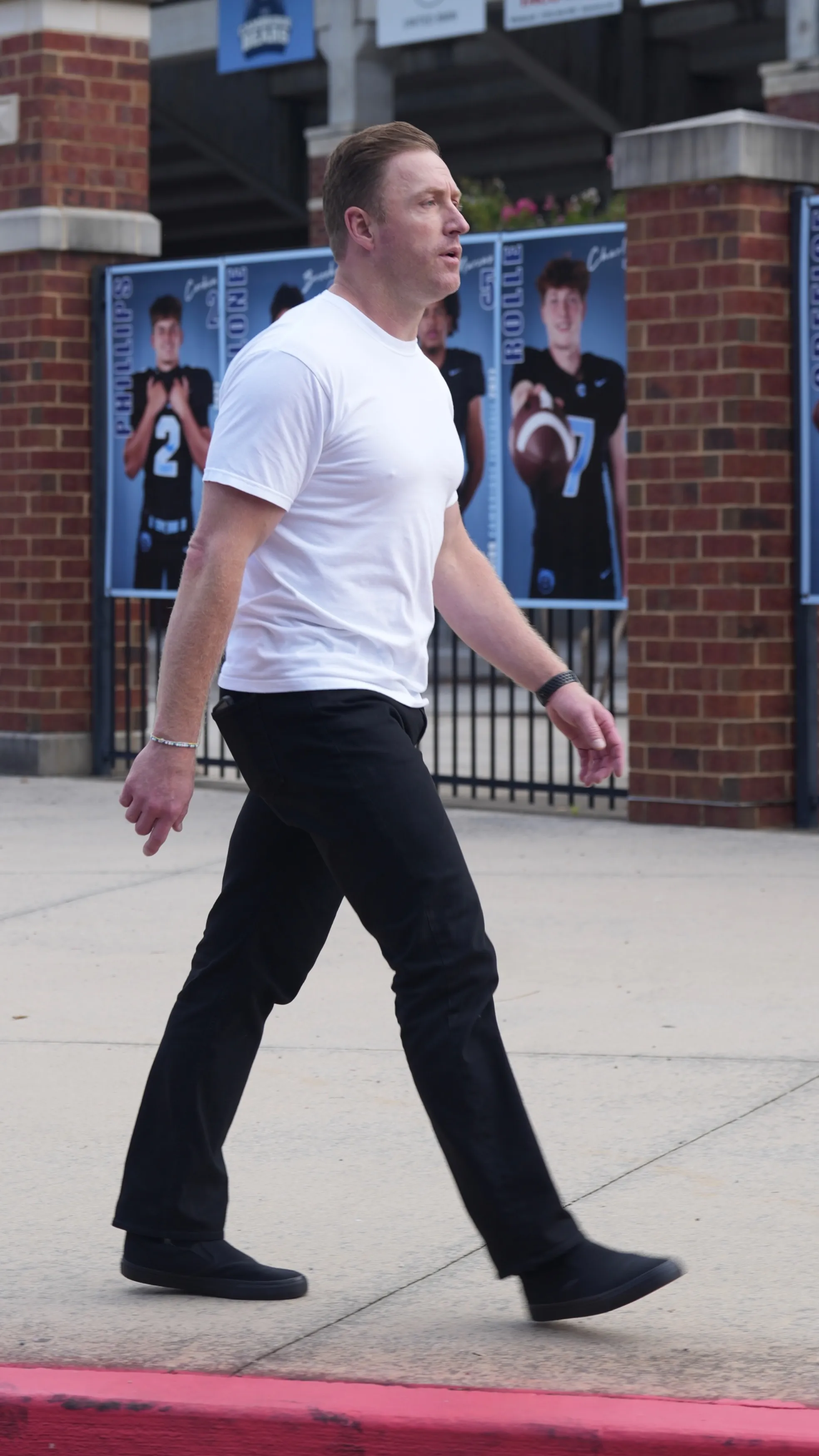 Kroy Biermann walking in a white t-shirt and black pants with football player banners in the background.