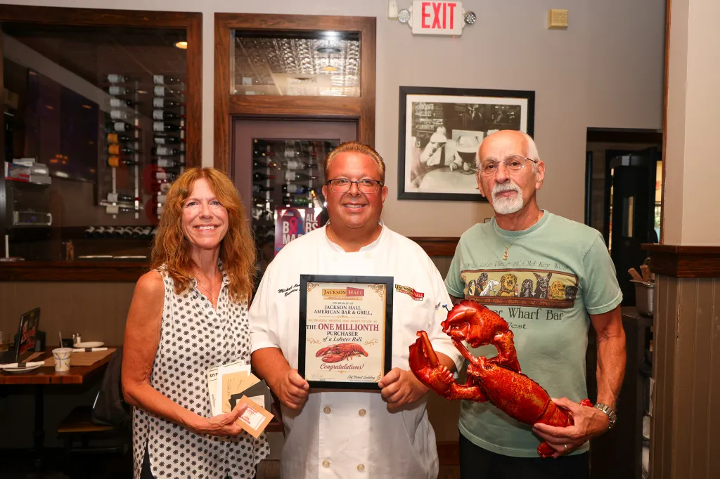 Three people pose in a restaurant, celebrating the sale of the one millionth lobster roll.