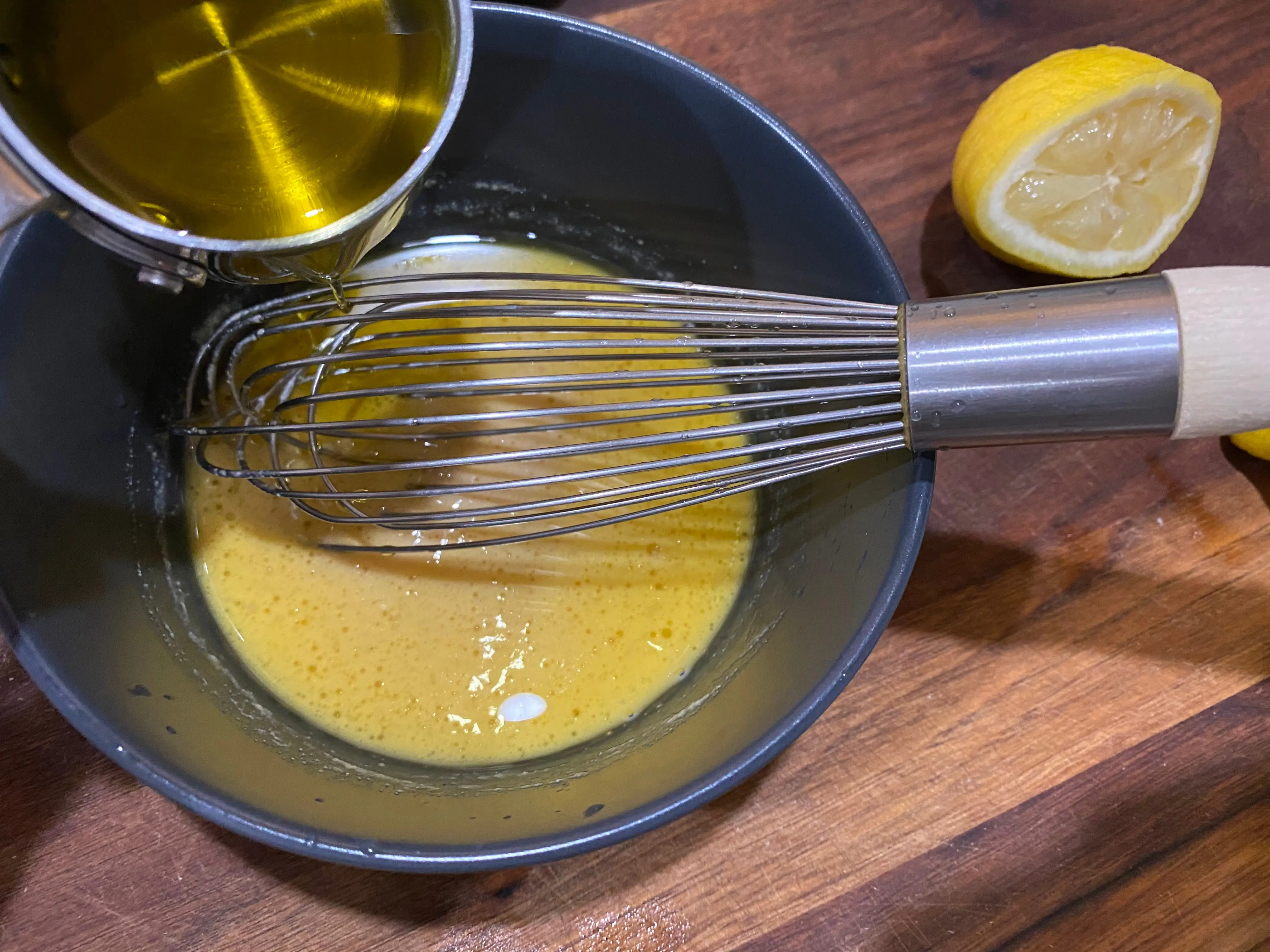 whisk in bowl with olive oil being poured into bowl