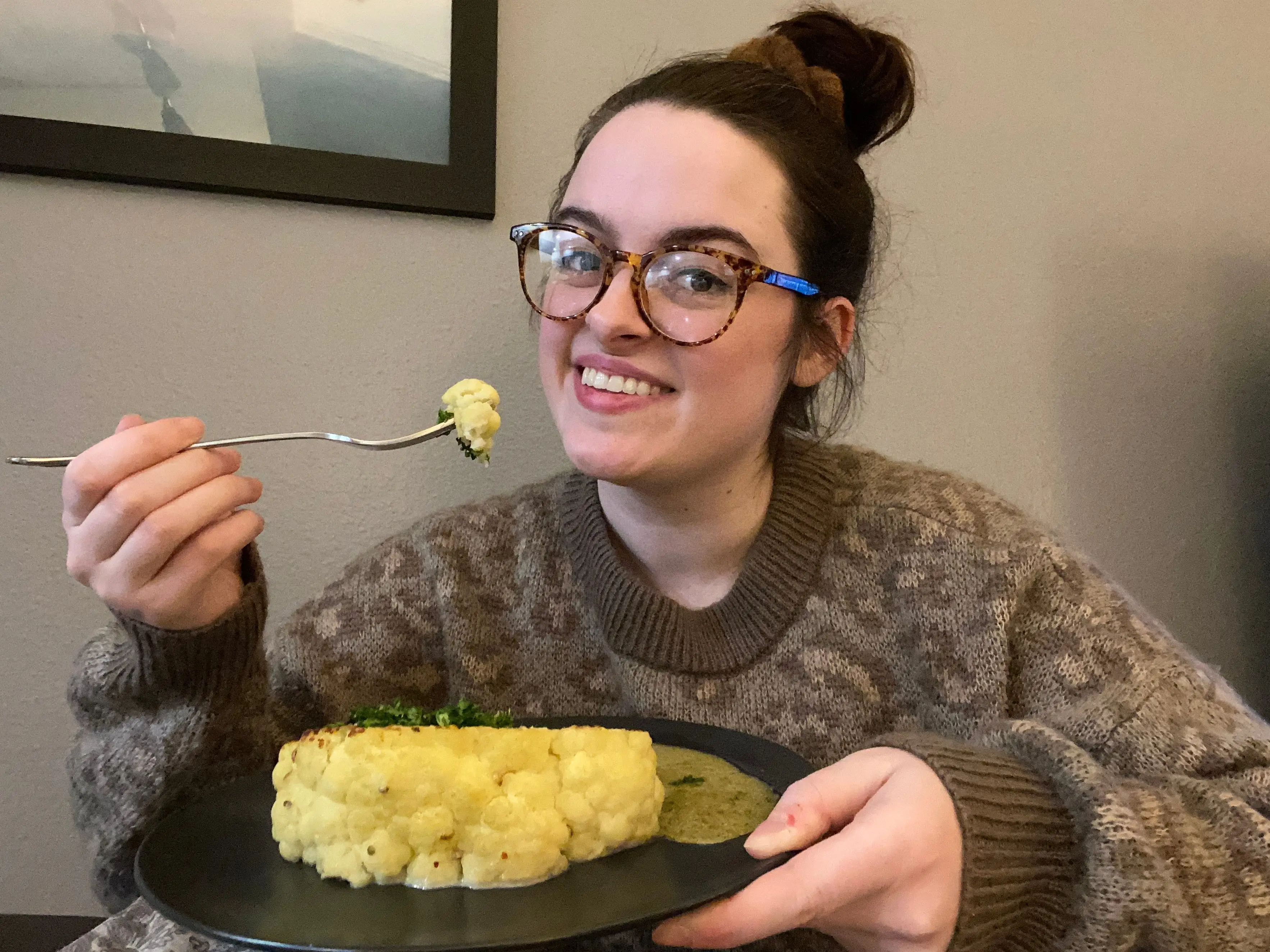 Woman smiling, holding caulfilower steak and bite of it on fork